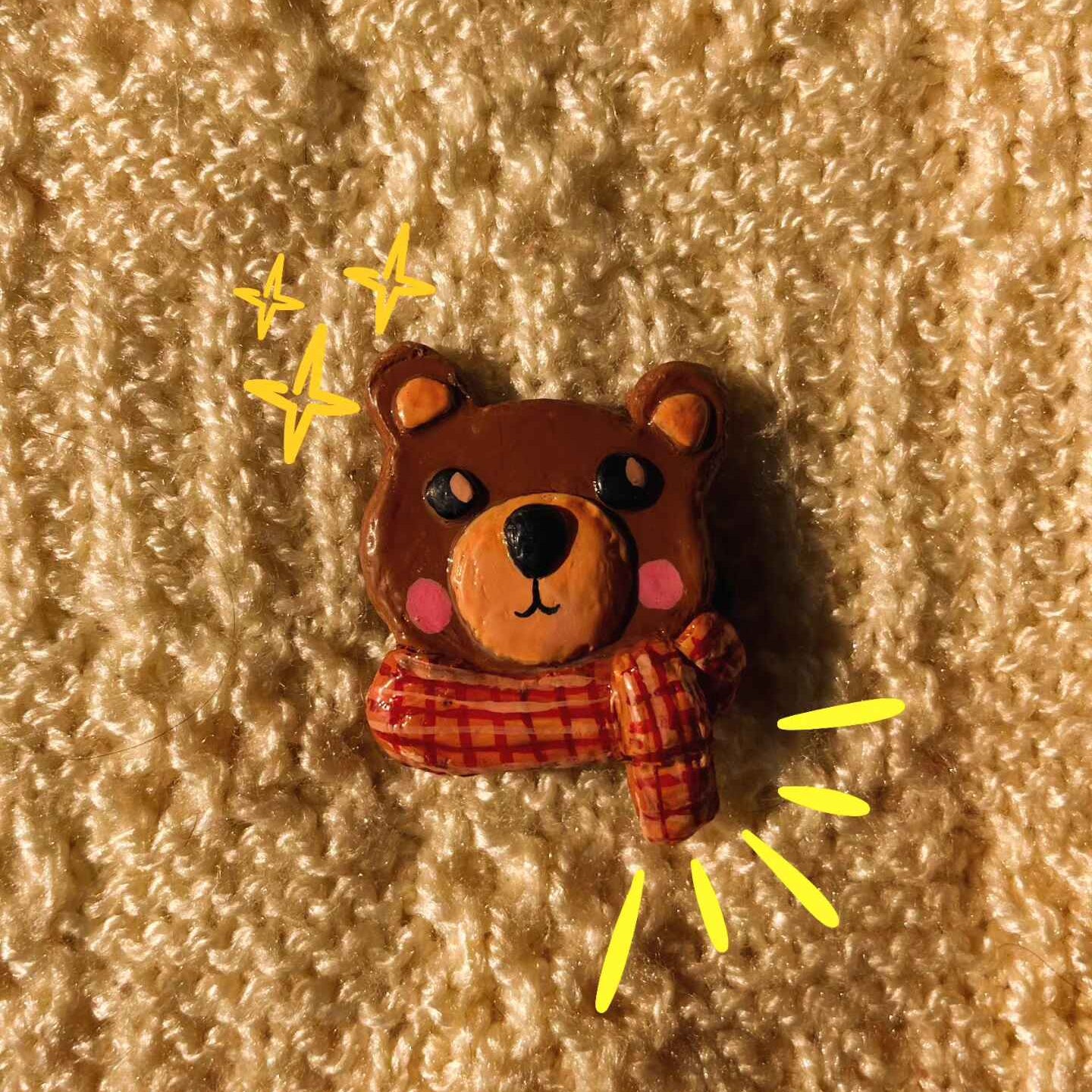 Bear-shaped object with a red scarf on a textured beige background