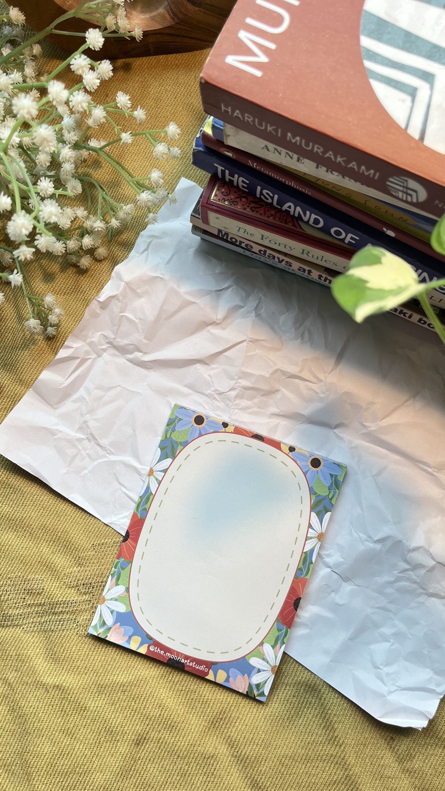 Colorful card with oval design on textured paper, surrounded by books and flowers.