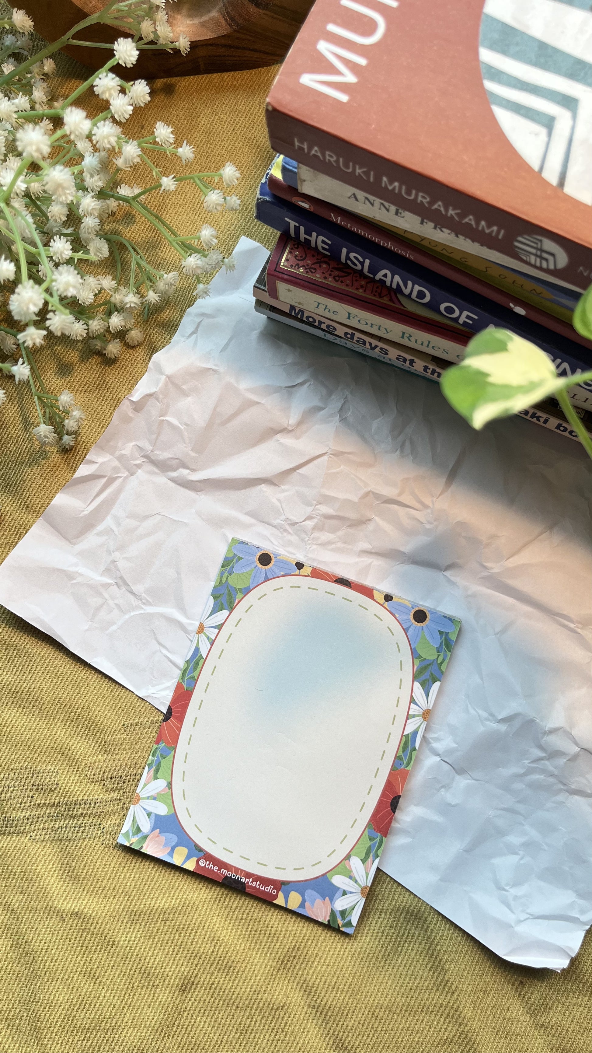 Colorful card with oval design on textured paper, surrounded by books and flowers.