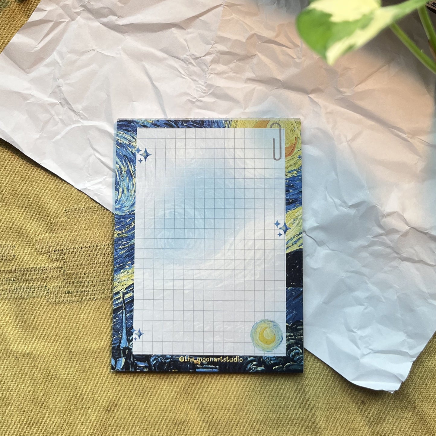 Notepad with grid on a textured surface with books and flowers in the background